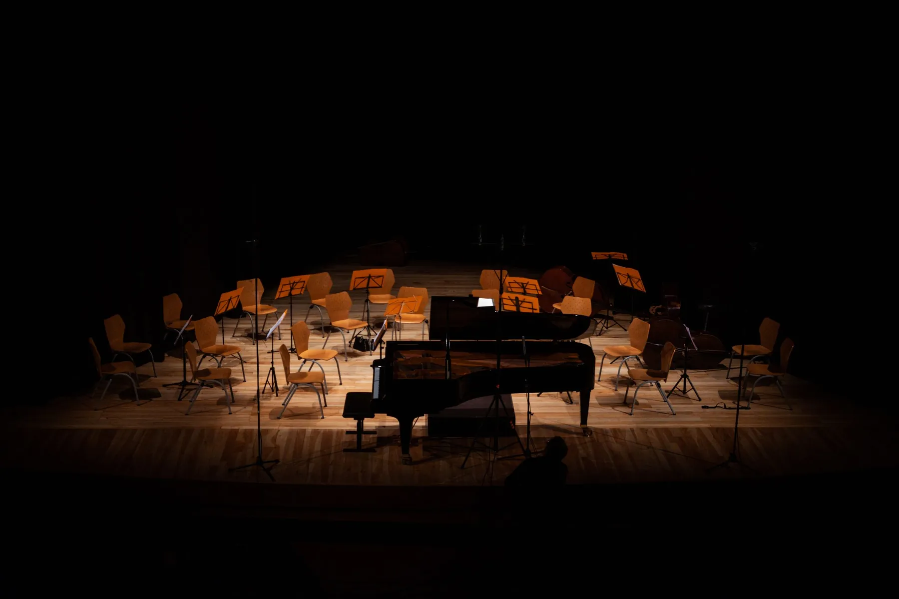 A grand piano on a dim stage with chairs and music stands waiting for a concert