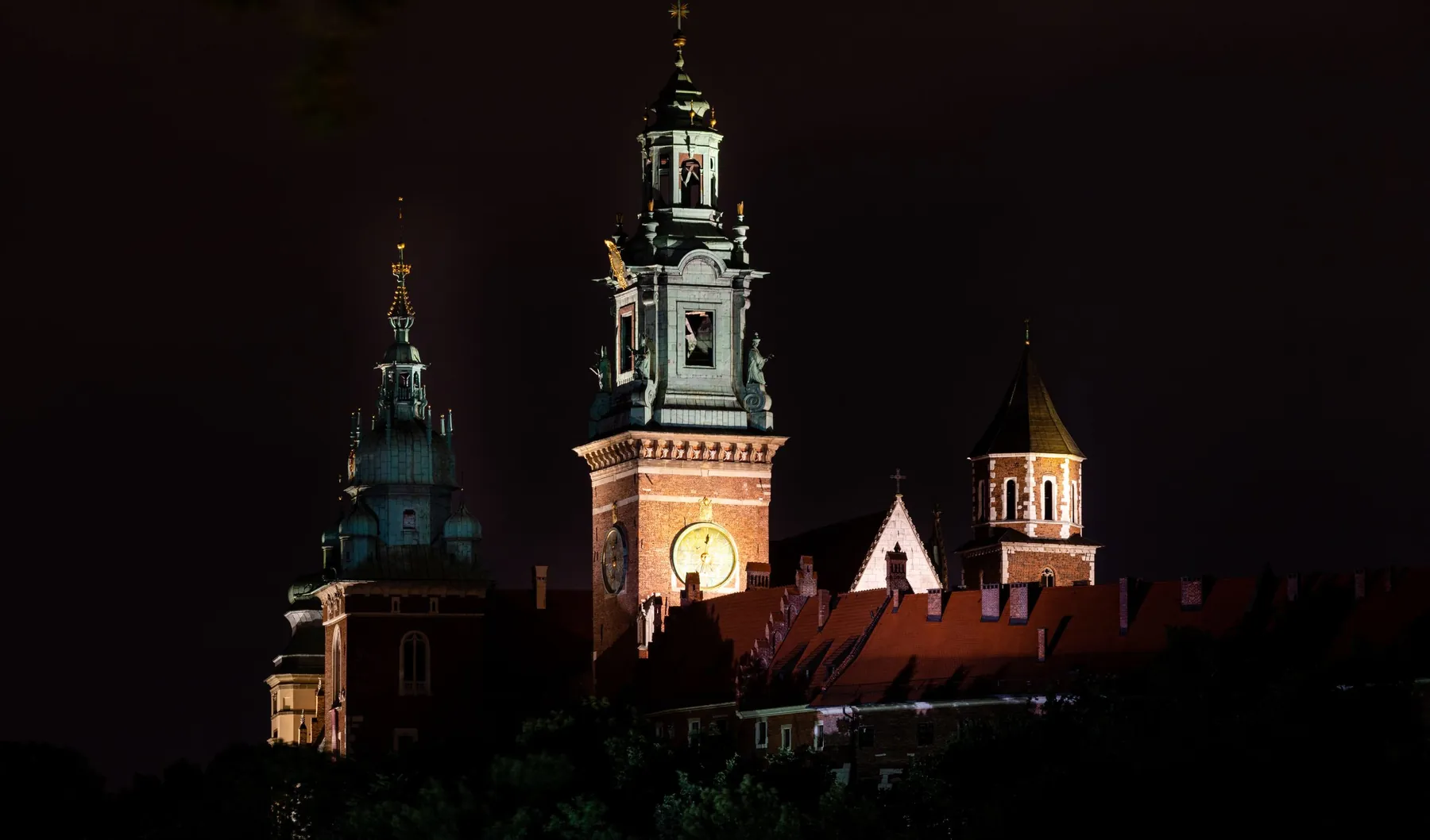 The towers and roofs of Wawel Castle floodlit against a black night sky